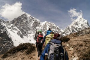 Group of hikers trekking on a sunny day with snow-capped mountains in the background. Outdoor adventure scene.