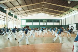 A large group engaged in a dynamic capoeira session indoors, emphasizing movement and teamwork.